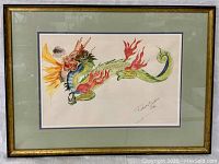 Framed watercolor artwork showing full dragon image with flames and signature, matted in green and framed in wood.