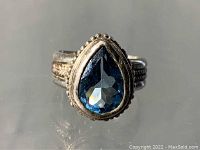 Close-up front view of the ring showing the pear-shaped blue faceted aquamarine stone set in sterling silver with beaded bezel.