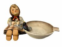 Front and side view of vintage Hummel ceramic ashtray with seated girl figurine holding bird attached to the ashtray dish.