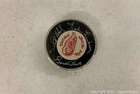 Top side of the puck showing Detroit Red Wings logo and multiple live ink signatures in silver/white ink, inside clear plastic case.