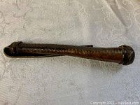 Dark brown leather baton on white textured fabric background, showing woven leather texture and reinforced ends.