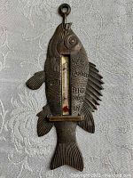 Front view of the dark metal fish-shaped thermometer with clear scale and embossed text on the metal surface.