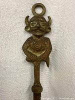 Close-up of the devil figure handle on the iron fire poker, showing facial features, horns, and loop for hanging