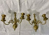 Front view of the pair of brass wall-mounted candle holders showing two arms each and the central mounting plate with loop.