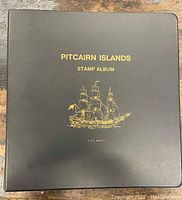 Black hardcover Pitcairn Islands stamp album with gold embossed ship illustration and text.