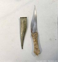 Full view of vintage bone-handled cutting tool with curved blade next to decorated sheath
