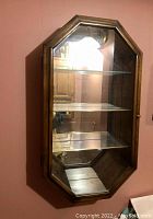 Front view of octagonal wooden hanging curio cabinet showing shape, glass shelves, and mirrored back.