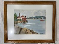 Frontal photo of the watercolor painting framed, showing harbor scene with rocks, brick building, sailboat, and hills.
