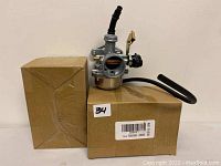 Photo showing two carburetors placed on cardboard boxes, highlighting the product with packaging underneath.