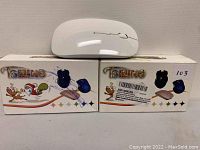 Two white wireless computer mice displayed on top of their original boxes. The boxes feature colorful graphics and images of the mice.