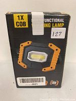 Box of a multifunctional working lamp with a single COB LED shown on the front, black and orange exterior, barcode visible.