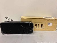 Front view of black digital alarm clock showing LED time display along with original box behind it.