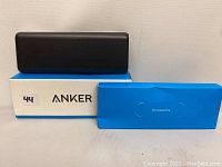 Black Anker power bank atop original white and blue box with blue accessory box beside it