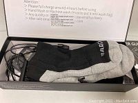 Black and gray heated socks in packaging with charger cable visible, showing size and packing information.
