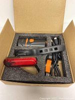 Bicycle light set inside foam-lined cardboard box showing front light, rear light, mounting straps, charging cable, and safety strap.