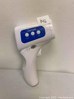 White digital non-contact infrared thermometer with three buttons and a handle, showing side profile with brand name 'Dearcom'.