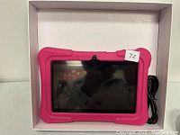 Photo of DragonTouch Kids Tablet with pink protective case and black charging cable coiled beside it in the box.