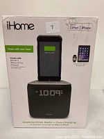 Front view of iHome docking clock radio box showing device charging an iPhone displaying 100% charge. Branding and key features visible including compatibility with iPhone 8, 8 Plus, and X.