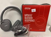 MPOW H7 over-ear Bluetooth headphones in black color with the original red MPOW packaging box. Includes USB charging cable and audio cable in a plastic bag.