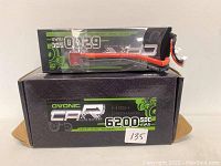 Two OVONIC 2S 7.4V 6200mAh 50C LiPo batteries on a box showing front label info including capacity, voltage, and discharge rating.