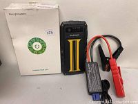 Ravpower jump starter device, original box, and jump start cable with clamps placed side by side on a white surface.