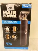Front of the box showing Teamyo brand, model T2, and features of the hair clipper including T-blade, USB charge, metal tube, and on/off switch.