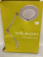 Yellow branded box showing an illustration of the Youkoyi LED desk lamp with adjustable arm and circular light head, secured by clamp base.