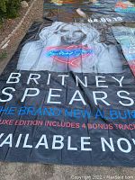 Photo of large black vinyl tarp featuring Britney Spears promotional image and album text laid flat on ground.