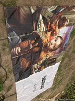 Full view of large vinyl tarp showing photographic image of person in brown sweater with children in background, folded with some wrinkles