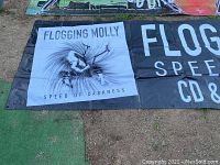 Close-up photo of the Flogging Molly tarp section showing band name and album artwork 'Speed of Darkness' with figure and dynamic hair illustration in black and white.