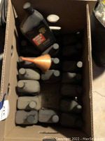 View from above into cardboard box containing multiple black plastic bottles of Dexron III Mercon transmission fluid and an orange funnel.