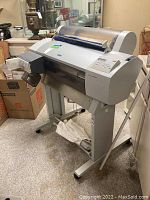 Side angle view of Epson Stylus Pro 7600 printer on stand with ink cartridges and power cable visible.