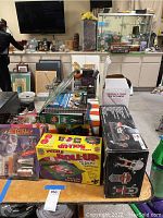 Photo showing the full lot on a table including boxed games, puzzles, painted makeup, novelty phones, and a boxed Baseball & Tennis pitcher.