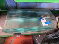Stack of clear glass panes on a green shelf with various dimensions visible.