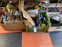 Two boxes with assorted household supplies including cleaning products, hand tools, and plumbing parts