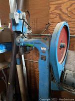 Side view of blue Ideal Wire Stitcher industrial stapler showing red flywheel and overall structure.