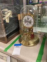 Full view of the Kundo anniversary clock under glass dome on brass base, showing overall condition and components.