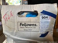 Photo of cardboard box labeled as containing tiles, with handwritten and printed notes describing the items inside: a Mark Goldfish enameled clear bowl, 1 cobalt blue-handled fish plate, 9 cobalt blue glass plates, and more cobalt blue items.