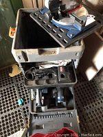 View of open toolbox containing charger, drill, and compartments for saws.