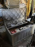 Open Suncast resin chest showing contents including vintage portable color TV, batteries, and other components inside.