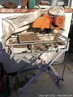 Tile saw angled view showing overall frame, motor, cutting table, and wheels.