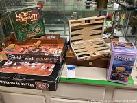 Overview photo of all items in the lot showing the Trivial Pursuit game, backgammon set, chess box, Lost in a Jigsaw II puzzle, and the 1000 piece puzzle tin.