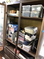 Wooden shelving unit containing various boxed items, a box fan, and loose goods in plastic bins.