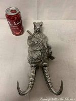Front angle of the Arthur Court rabbit coat hook next to soda can for scale, showing detailed metalwork and two curved hooks forming the legs.