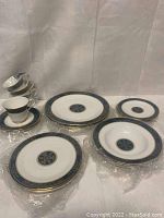 Overview of 24-piece Carlyle pattern place settings in plastic sleeves, including plates, bowls, cups and saucers.