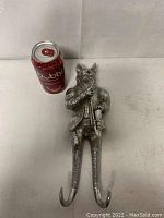 Front view of cast metal fox coat hook standing upright next to soda can for scale. Shows the full figure with two curved hooks extending downwards.