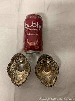 Pair of oval footed nut dishes beside soda can for scale. Both have scalloped edges and intricate cutout patterns.