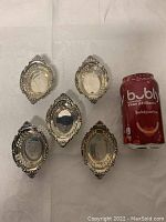 Five oval-shaped antique nut dishes arranged next to a soda can for size reference. Each dish has ornate edges and decorative pierced sides.