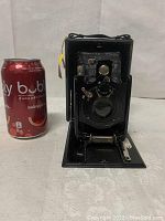 Front view of antique Kuribayashi folding bellows camera next to soda can for scale