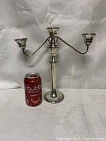 Full view of sterling silver three-arm candelabra beside a soda can for scale. The candelabra has a central column and three curved arms holding candle cups.
